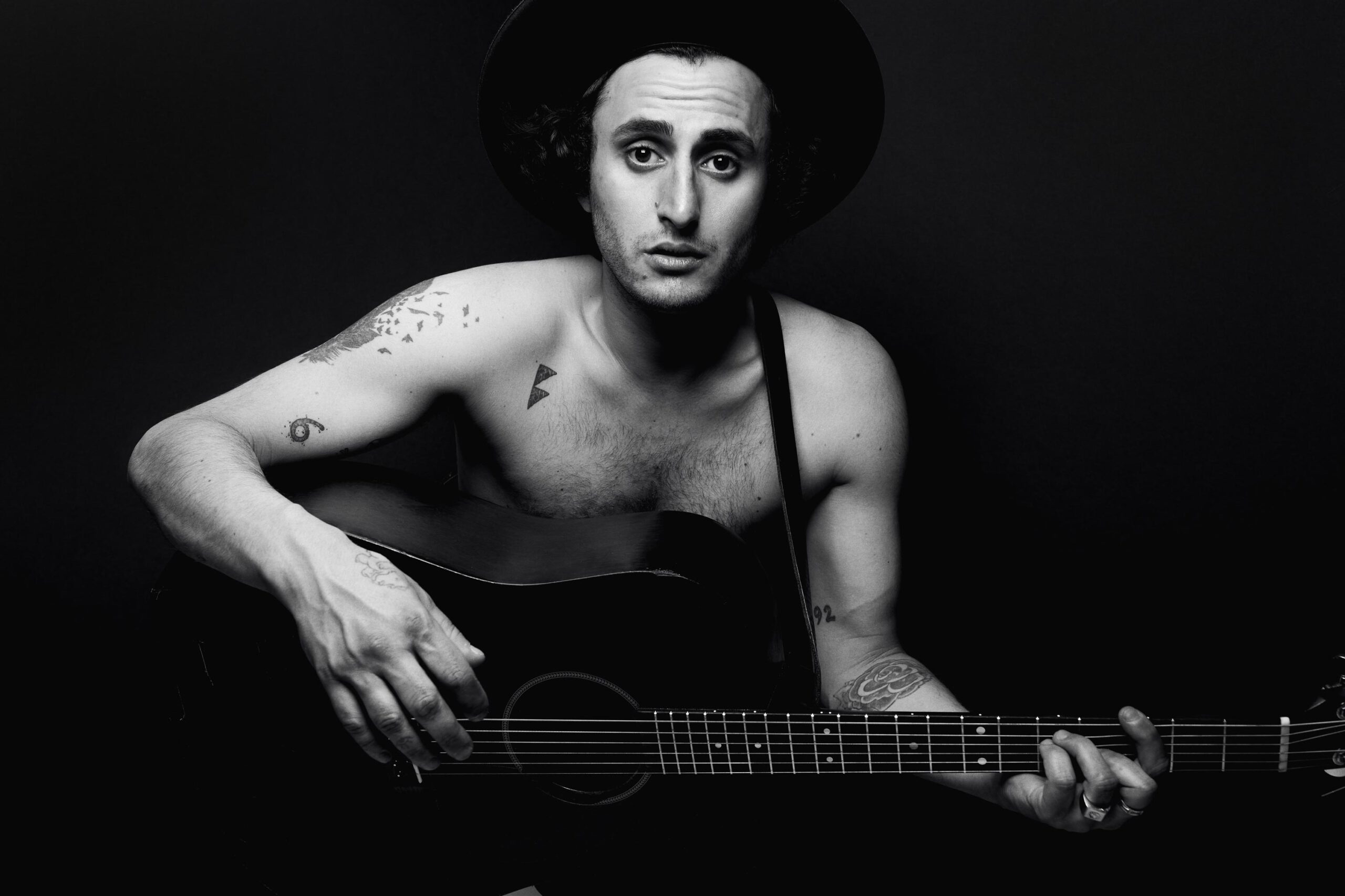 Portrait photographie de Rick Pagano en chest avec sa guitar sur fond noir. Photographe album musique à Montréal.