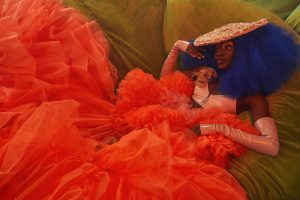 Model lying on green grass in a large orange tule dress