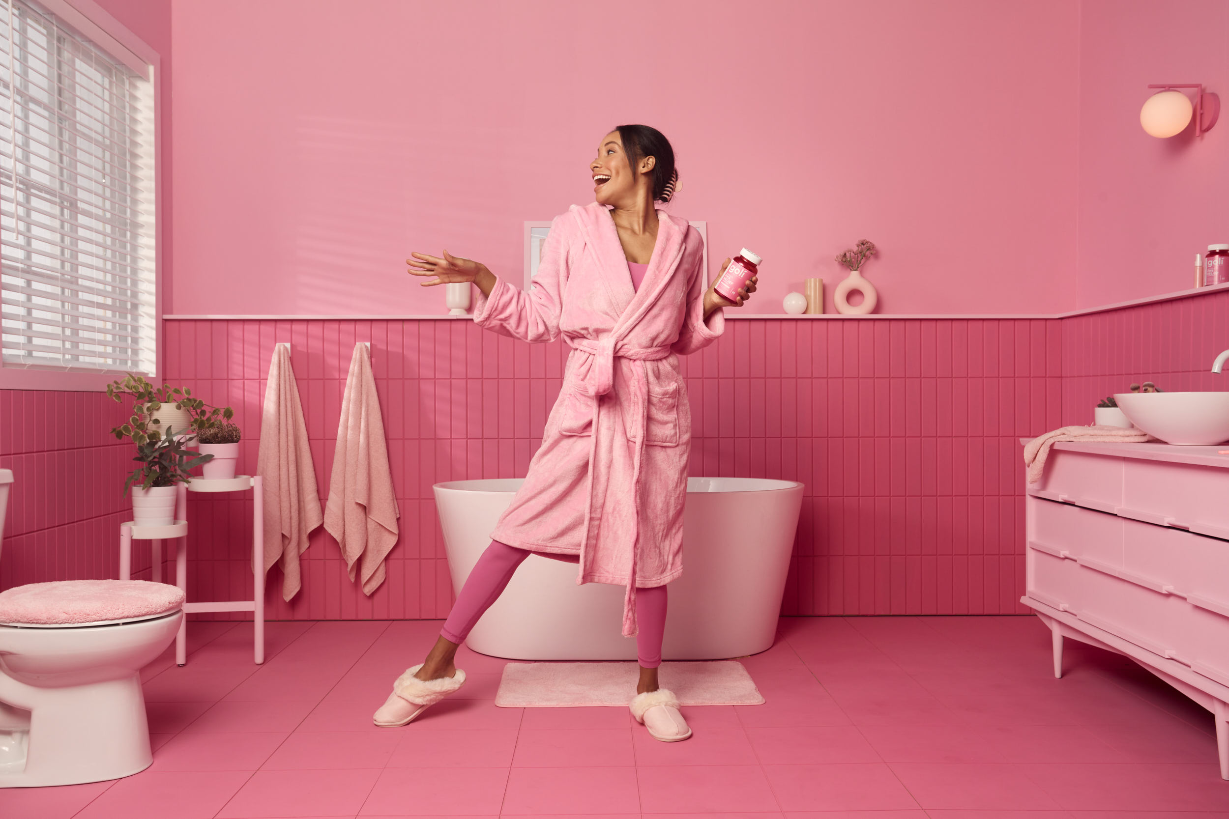 Photographie d'une femme en pijama qui danse dans une salle de bain complètement rose